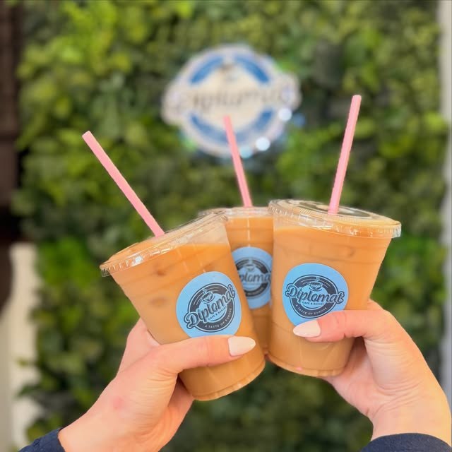 Three iced coffees held up in front of the shop